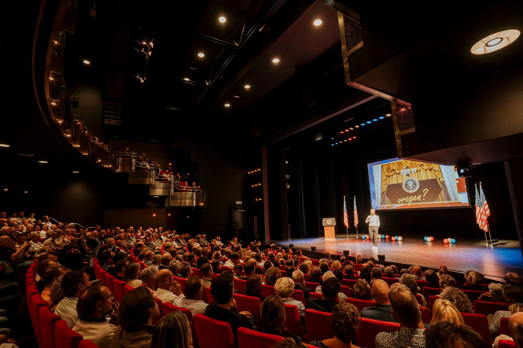Raymond op het podium voor een volle theaterzaal